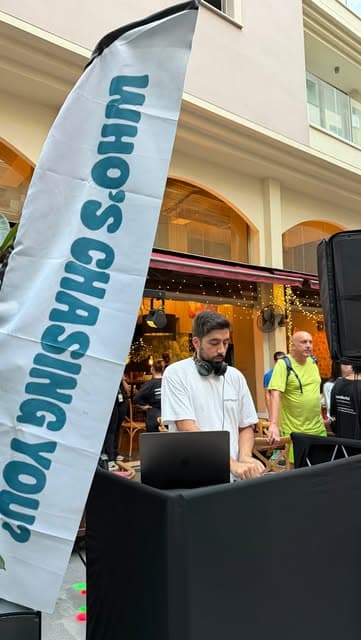 A DJ playing next to a Who's Chasing You flag at a post-run party